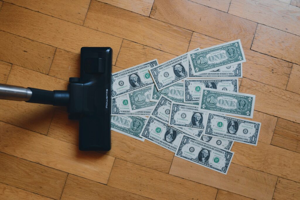 A vacuum cleaner sucking up various denominations of paper money from a carpet, symbolizing the rapid loss of financial resources due to high interest rates.
